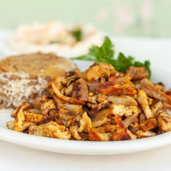 A plate of Habayit Restaurant's chicken shawarma with rice, pita bread, and parsley.