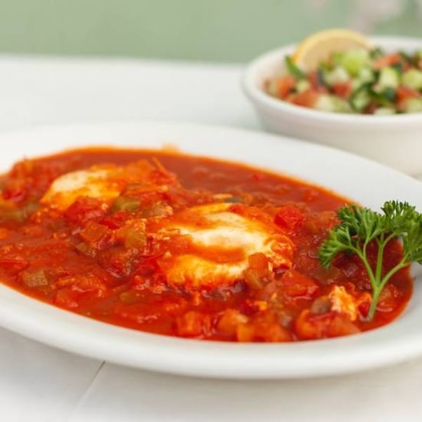 Shakshuka, a traditional Israeli dish, with two poached eggs in a rich tomato sauce, served with a side salad.