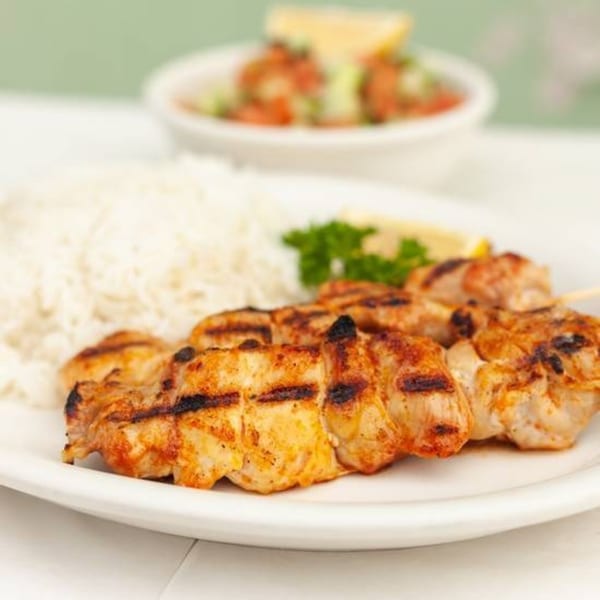Grilled chicken skewers with white rice, a lemon wedge, parsley, and a side salad.