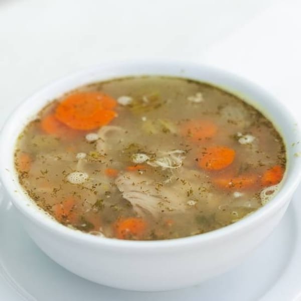 A white bowl of Habayit Restaurant's Israeli chicken soup with carrots, dill, and chicken pieces.